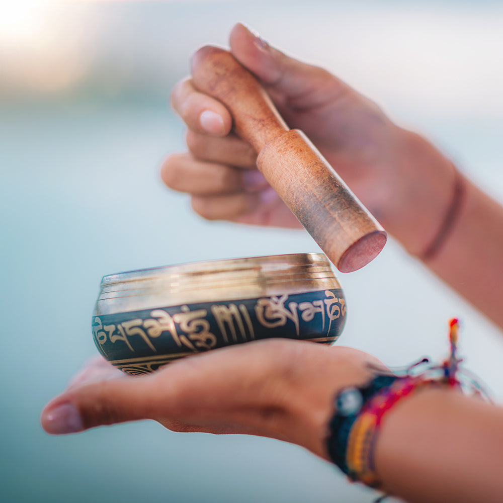 Woman doing yoga with Tibetan bracelets hitting singing bowl with wooden stick